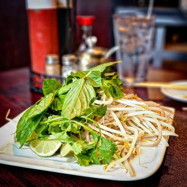Fresh herbs, bean sprouts, and lime wedges on a white plate, ready for Vietnamese phở.