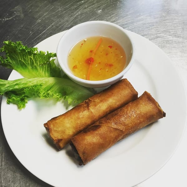 Two crispy Vietnamese spring rolls with lettuce and a dipping sauce on a white plate.