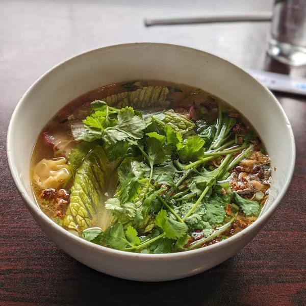 A white bowl of Vietnamese wonton soup with fresh cilantro, lettuce, and fried garlic.