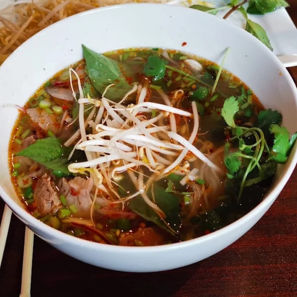 Close-up of a bowl of What The Phở's Vietnamese pho with beef, noodles, bean sprouts, and herbs.