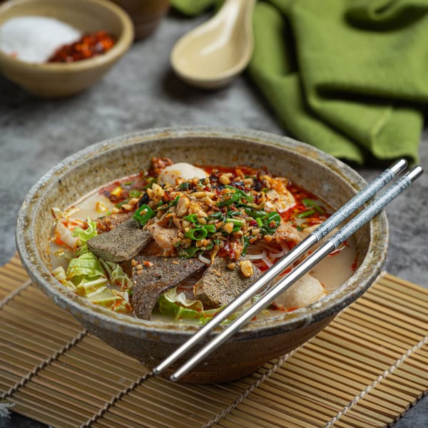 A bowl of Vietnamese phở with meat, noodles, and vegetables, garnished with peanuts and green onions.
