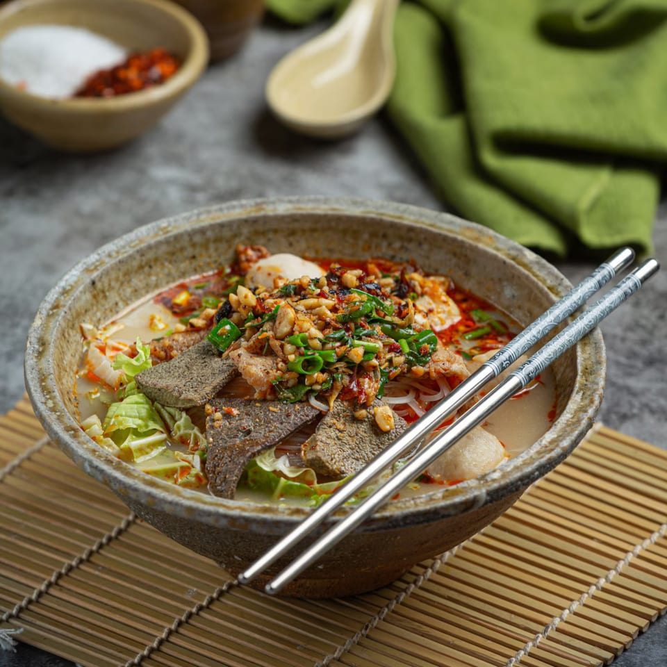 A bowl of Vietnamese phở with meat, noodles, and vegetables, garnished with peanuts and green onions.