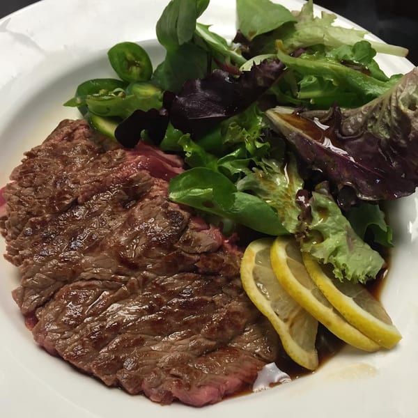 Grilled beef slices with a side salad, jalapenos, and lemon wedges on a white plate.