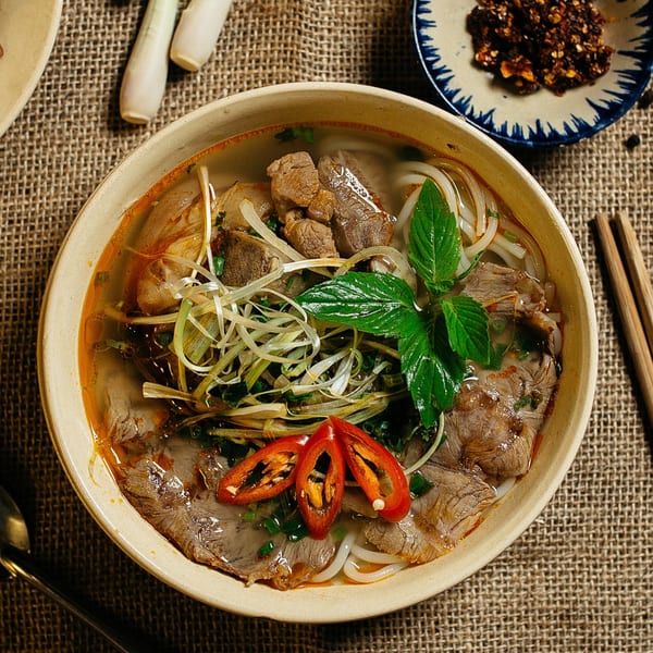 Overhead view of a bowl of Vietnamese pho with beef, noodles, herbs, and chili slices.
