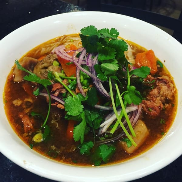 A close-up of a bowl of Vietnamese phở with beef, noodles, carrots, red onions, and cilantro.